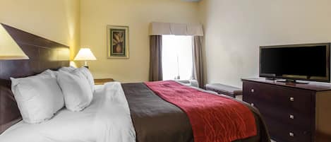 A hotel room with a bed, a television, a desk, and a window with curtains.