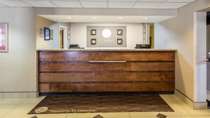 Un hall d’accueil d’hôtel avec un comptoir de réception en bois, une enseigne indiquant « Comfort Inns & Suites » et un paillasson.
