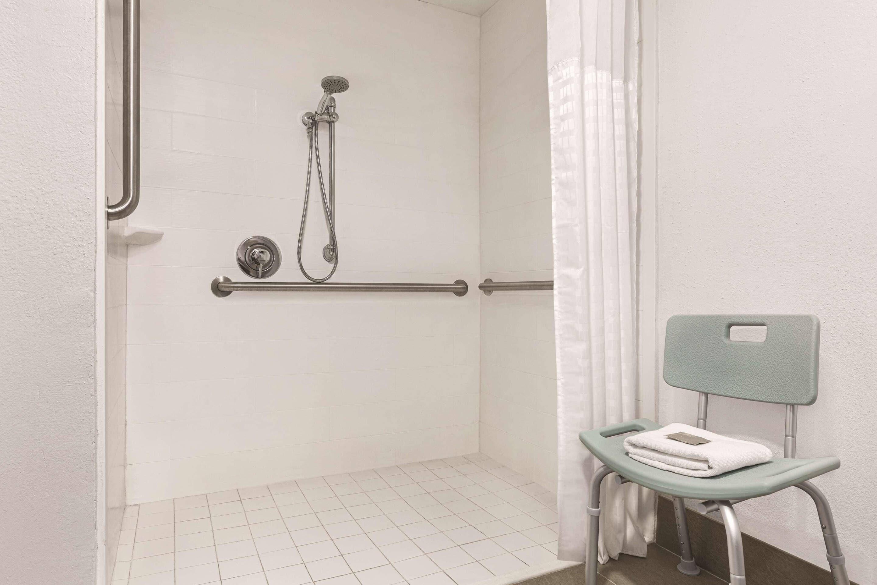 A shower area with a grab bar, a chair with a towel, and a showerhead.