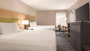 A hotel room with two beds, a desk, a television, and a seating area.