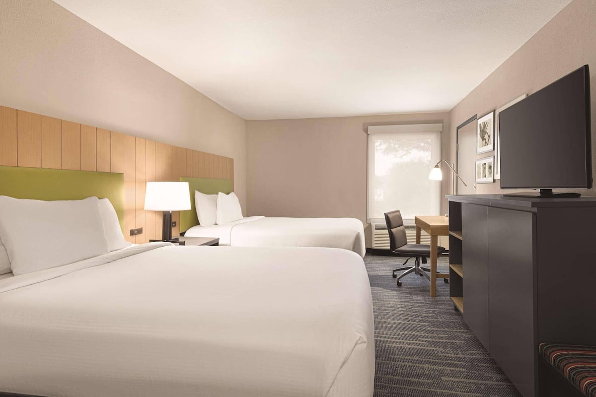 A hotel room with two beds, a desk, a television, and a seating area.
