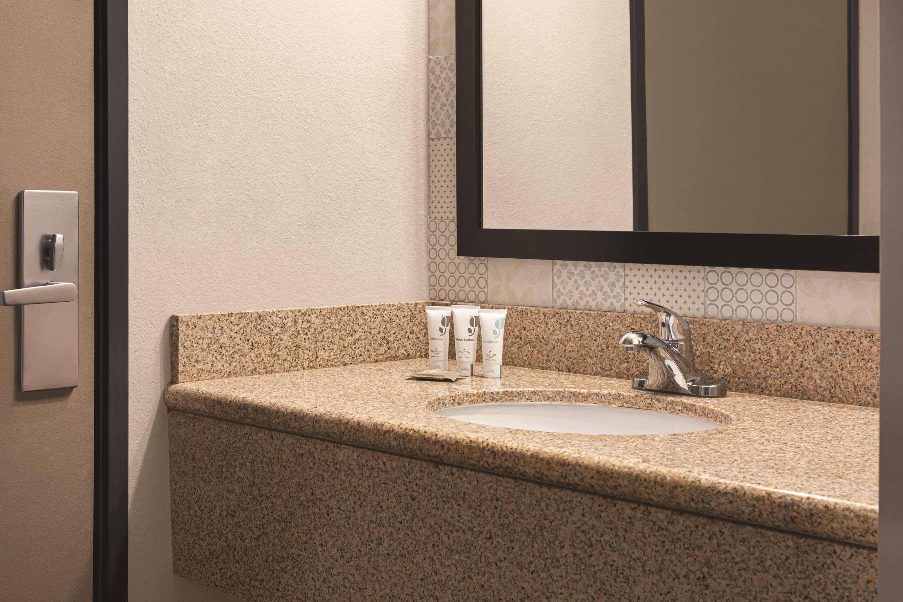 A bathroom with a granite countertop, a sink, a mirror, and a towel dispenser.