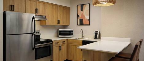A modern kitchen with stainless steel appliances, wooden cabinets, a white countertop, and a hanging light fixture.
