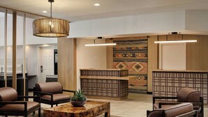 Un hall con sillones de cuero, una mesa de centro de madera con una planta y un mostrador de recepción con baldosas estampadas.