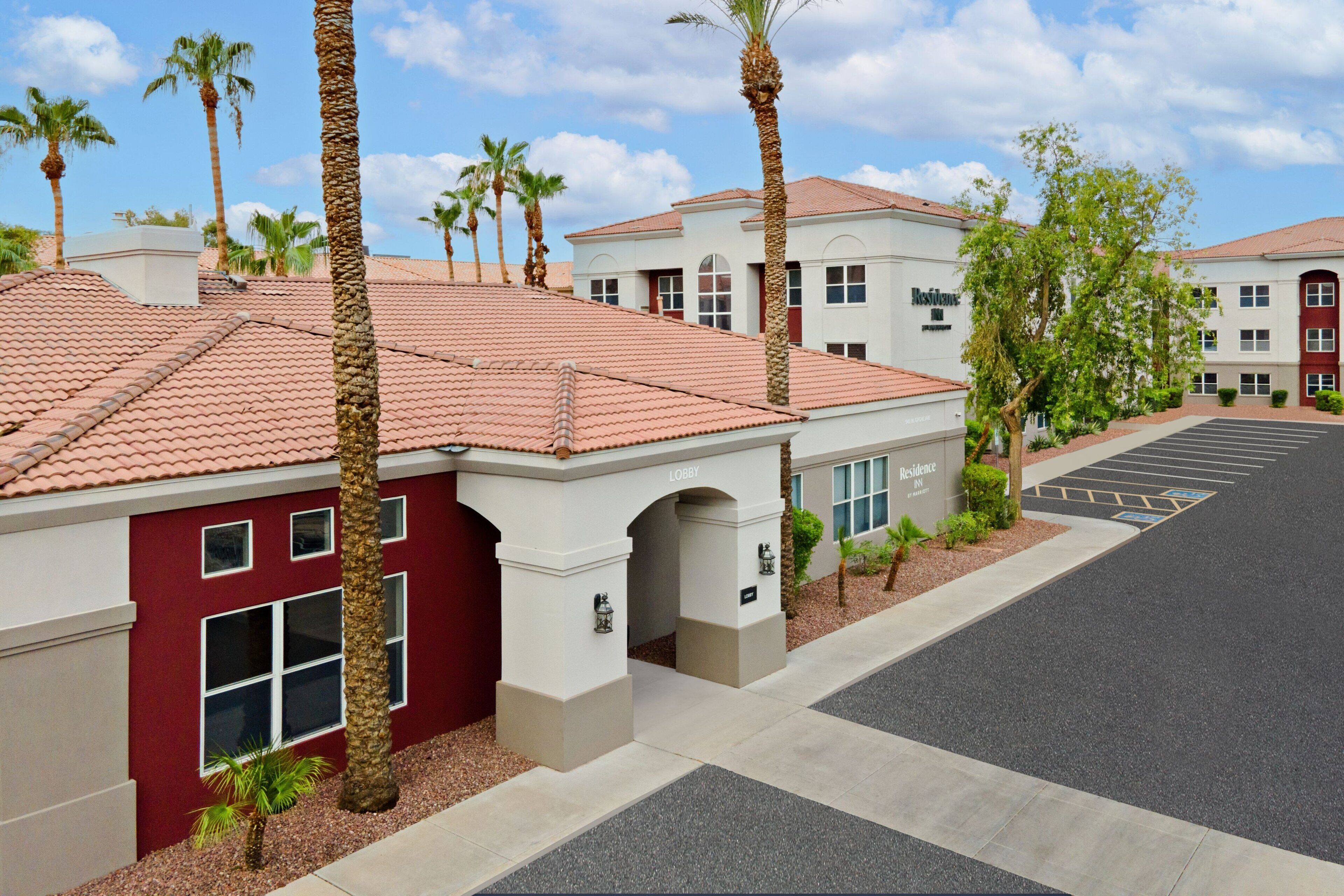 A hotel with a red-tiled roof, palm trees, and a parking lot.