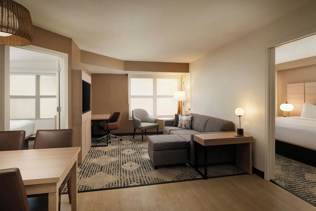 A hotel room with a bed, a sofa, a desk, a chair, and a TV.