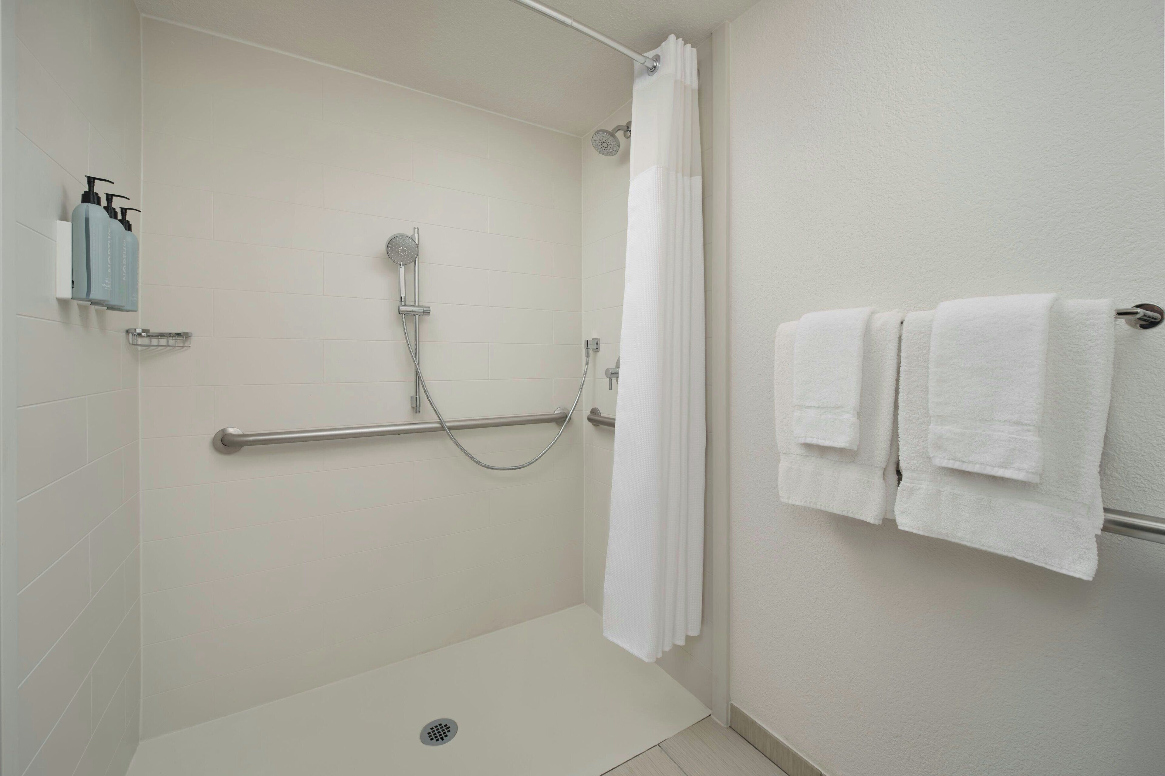 A shower area with a grab bar, a showerhead, and a towel rack with towels.