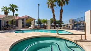 A swimming pool with a tiled edge, surrounded by palm trees and a building with a red roof.