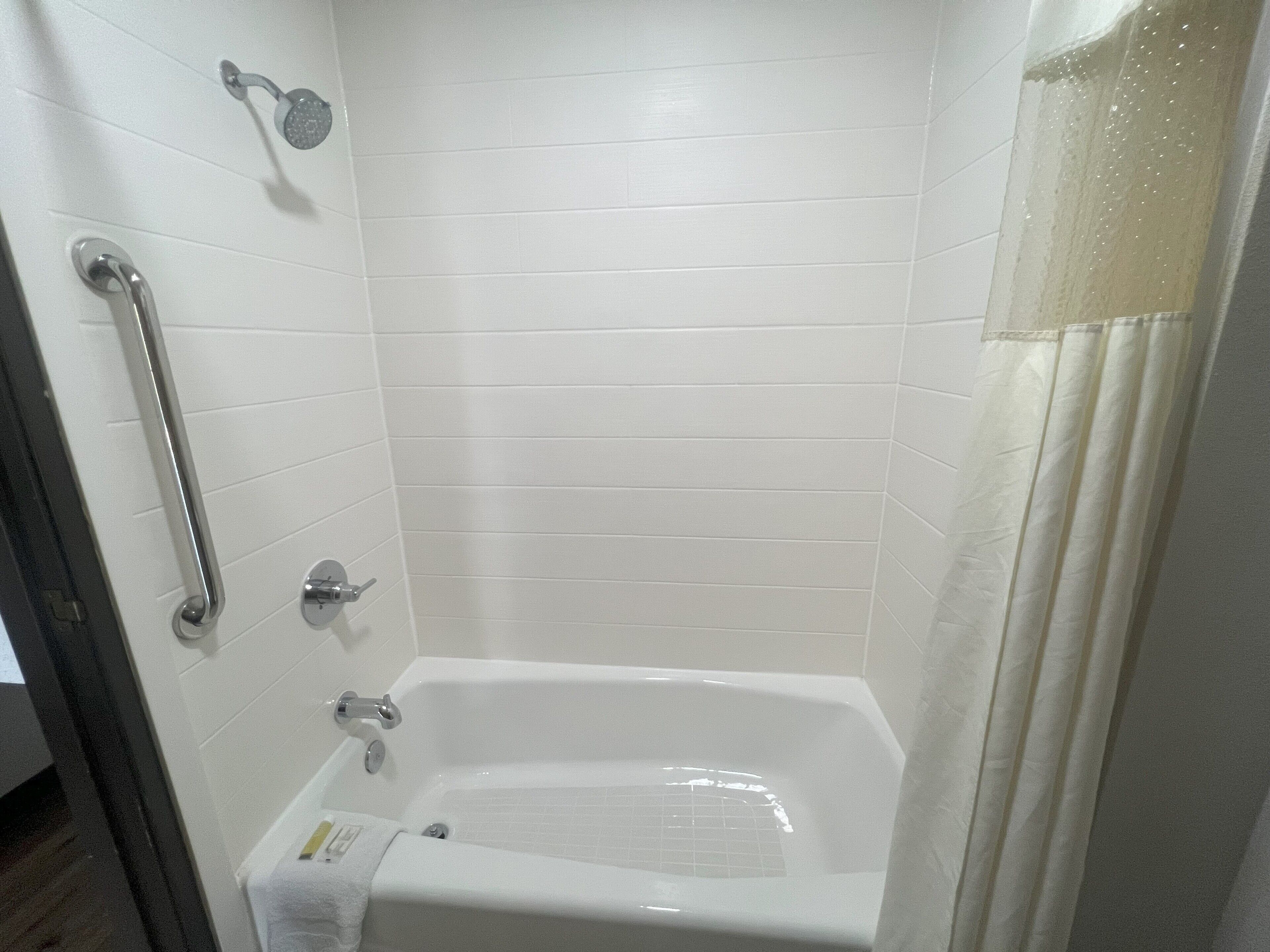 Un baño con una bañera blanca, una ducha con cabezal de ducha manual y una barra de apoyo en la pared.