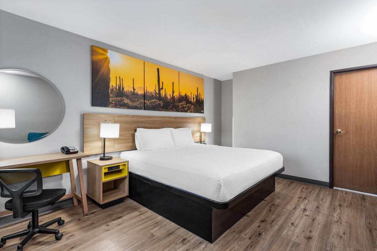 A hotel room with a bed, desk, chair, and a large painting on the wall.
