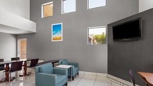 A modern dining area with a high ceiling, a flat-screen TV mounted on the wall, and a seating arrangement including a table and chairs.