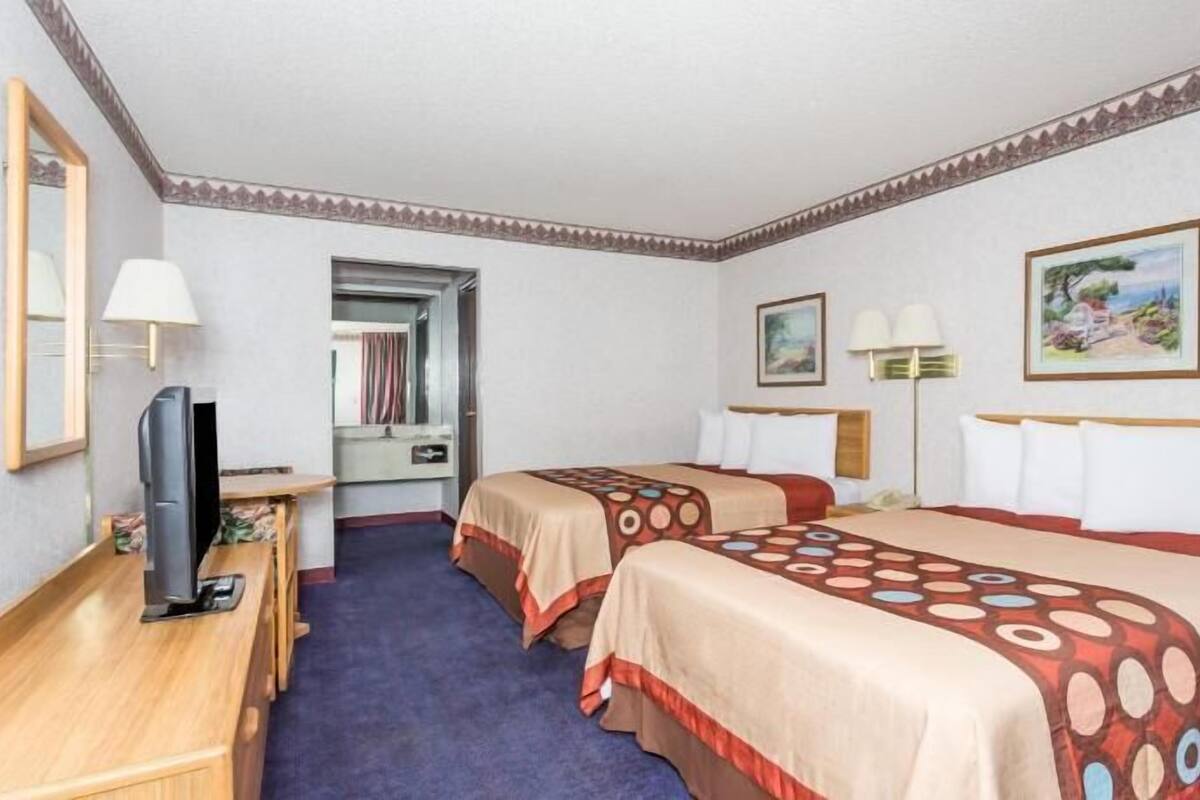A hotel room with two beds, a TV, a desk, and a mirror.
