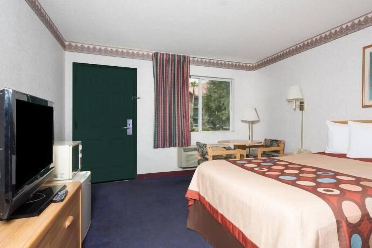 A hotel room with a bed, a desk, a television, a lamp, and a painting.