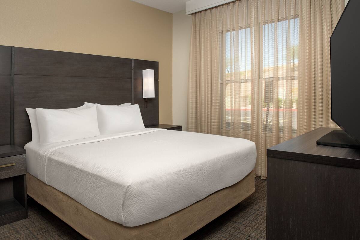 A hotel room with a large bed, a nightstand, a TV, and a window with curtains.