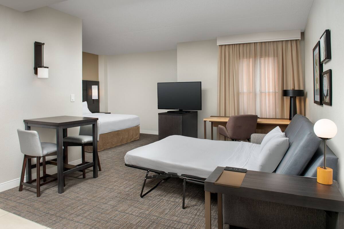 A hotel room with a bed, a desk, a chair, a television, and a lamp.