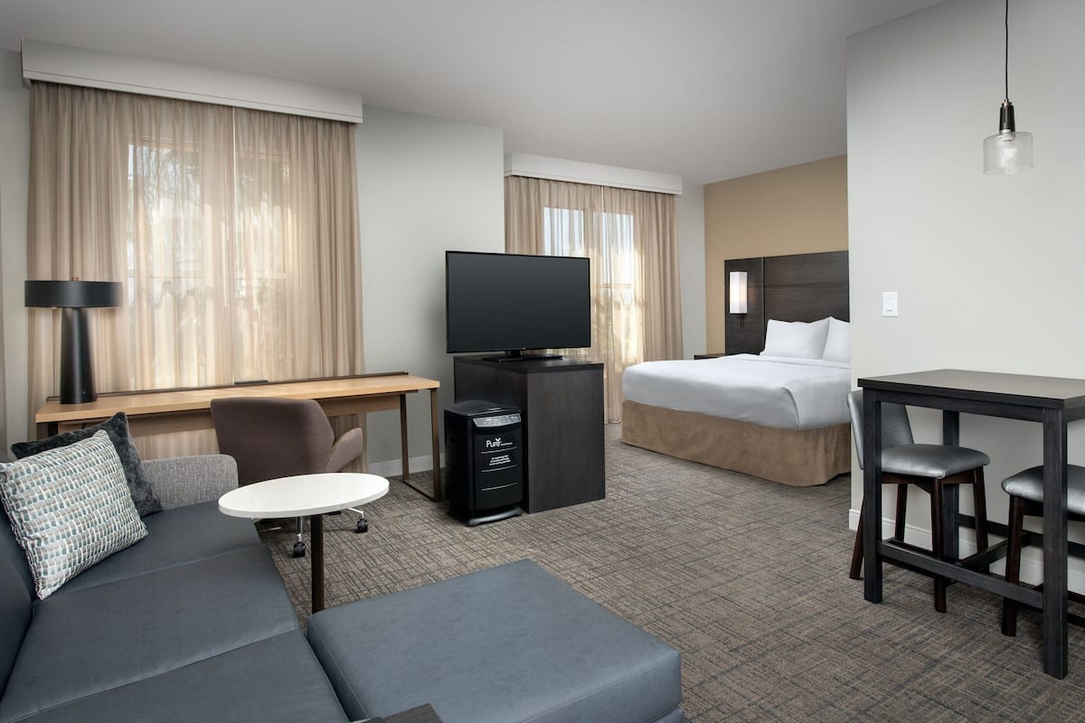 A hotel room with a sofa, a desk, a television, a bed, and a small table with two chairs.
