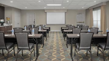 A conference room with a large screen, multiple tables, and chairs, equipped with water bottles.