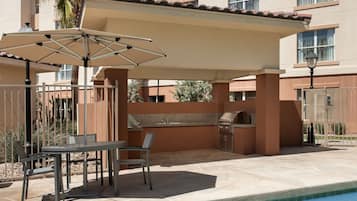 Un patio exterior con mesa y sillas, una parrilla y una piscina.