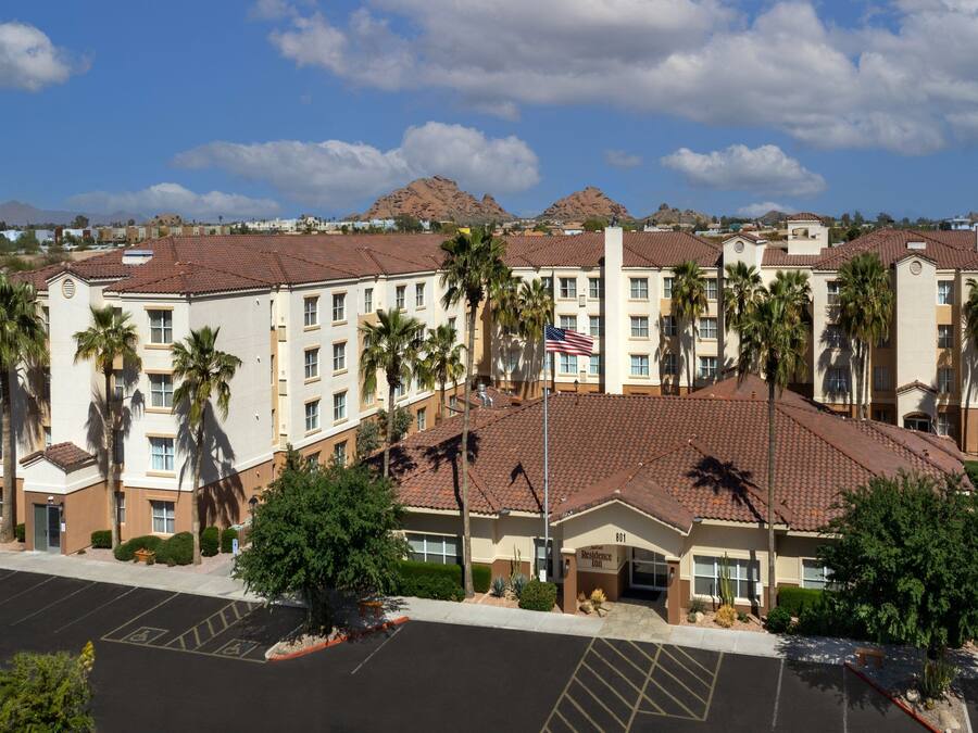 A multi-story hotel with a red-tiled roof, palm trees, and an American flag.