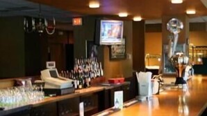 A bar area with a counter, glasses, and a television screen. - Maron Hotel And Suites (Danbury)