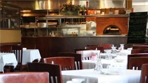 A restaurant with tables set for dining, a brick oven, and a menu board. - Maron Hotel And Suites (Danbury)