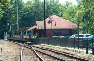 Una estación de tren con vías, un pequeño refugio y una valla.