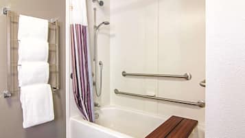 A bathroom with a white bathtub, a wooden shelf, and a towel rack with multiple towels.
