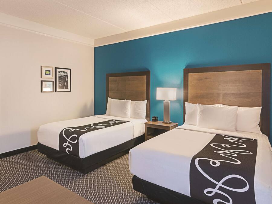 Ein Hotelzimmer mit zwei Betten, einem Nachttisch mit Lampe und gerahmten Bildern an der Wand.