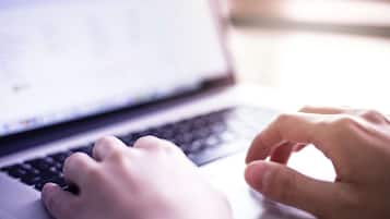 Primer plano de manos escribiendo en el teclado de una computadora portátil.