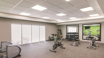 Un gimnasio con equipo de ejercicio, un espejo grande y una zona de entrenamiento verde.