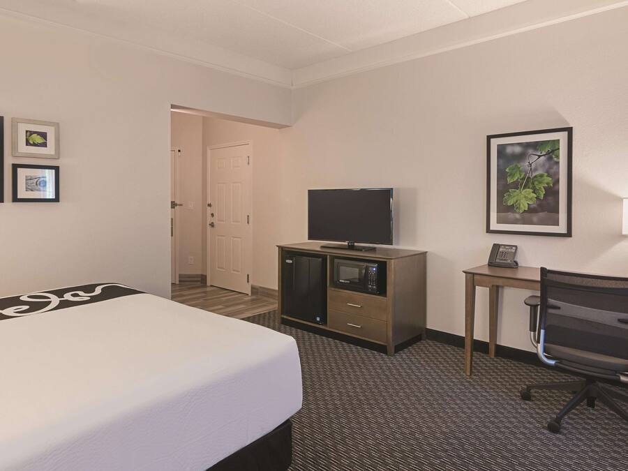 A hotel room with a bed, a desk with a chair, a television, and a microwave.