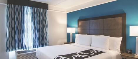 Habitación de hotel con una cama grande, dos lámparas de noche, cabecero y una ventana con cortinas estampadas.