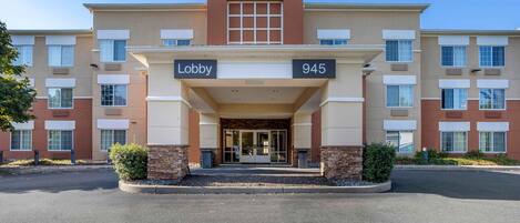 Un hotel Stay AmericA con entrada al vestíbulo, número 945, y un cartel que indica el área de recepción.