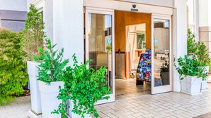 A hotel entrance with a glass door, automatic caution sign, and a small outdoor seating area with magazines.