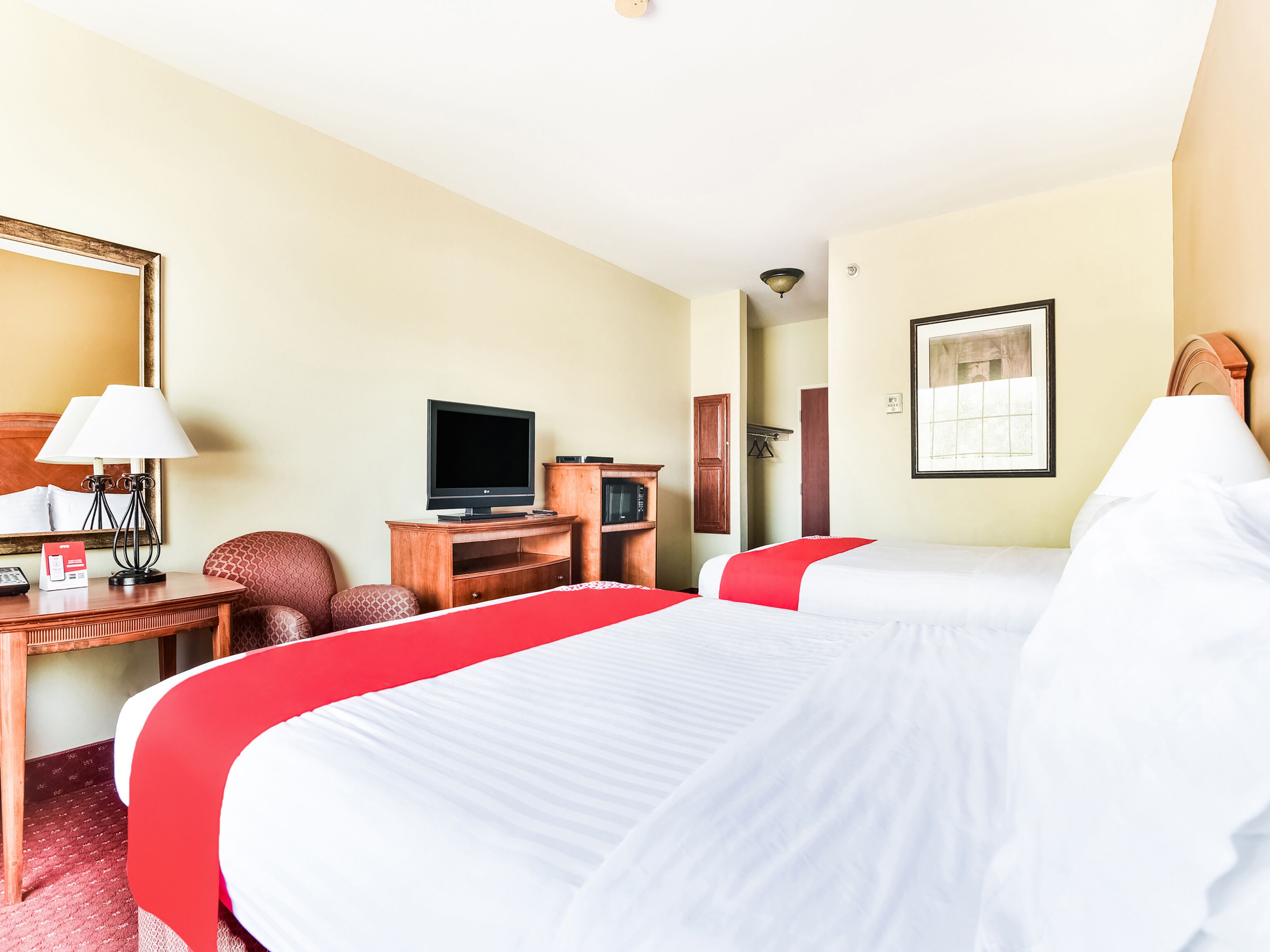 A hotel room with two beds, a desk with a television, a chair, and a mirror.