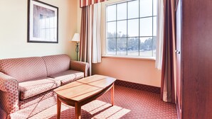 A room with a sofa, a table, a window with curtains, and a framed picture on the wall.