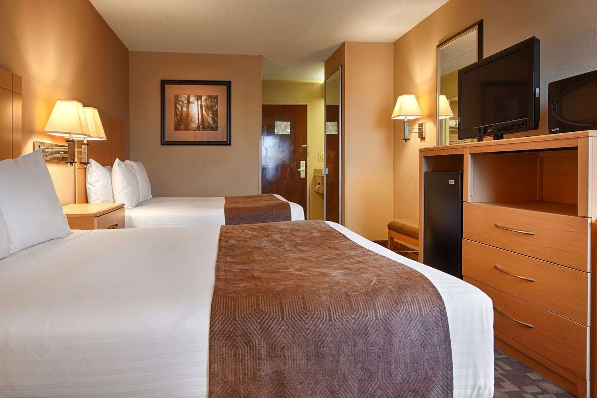 A hotel room with two beds, a TV, a desk, and a dresser.
