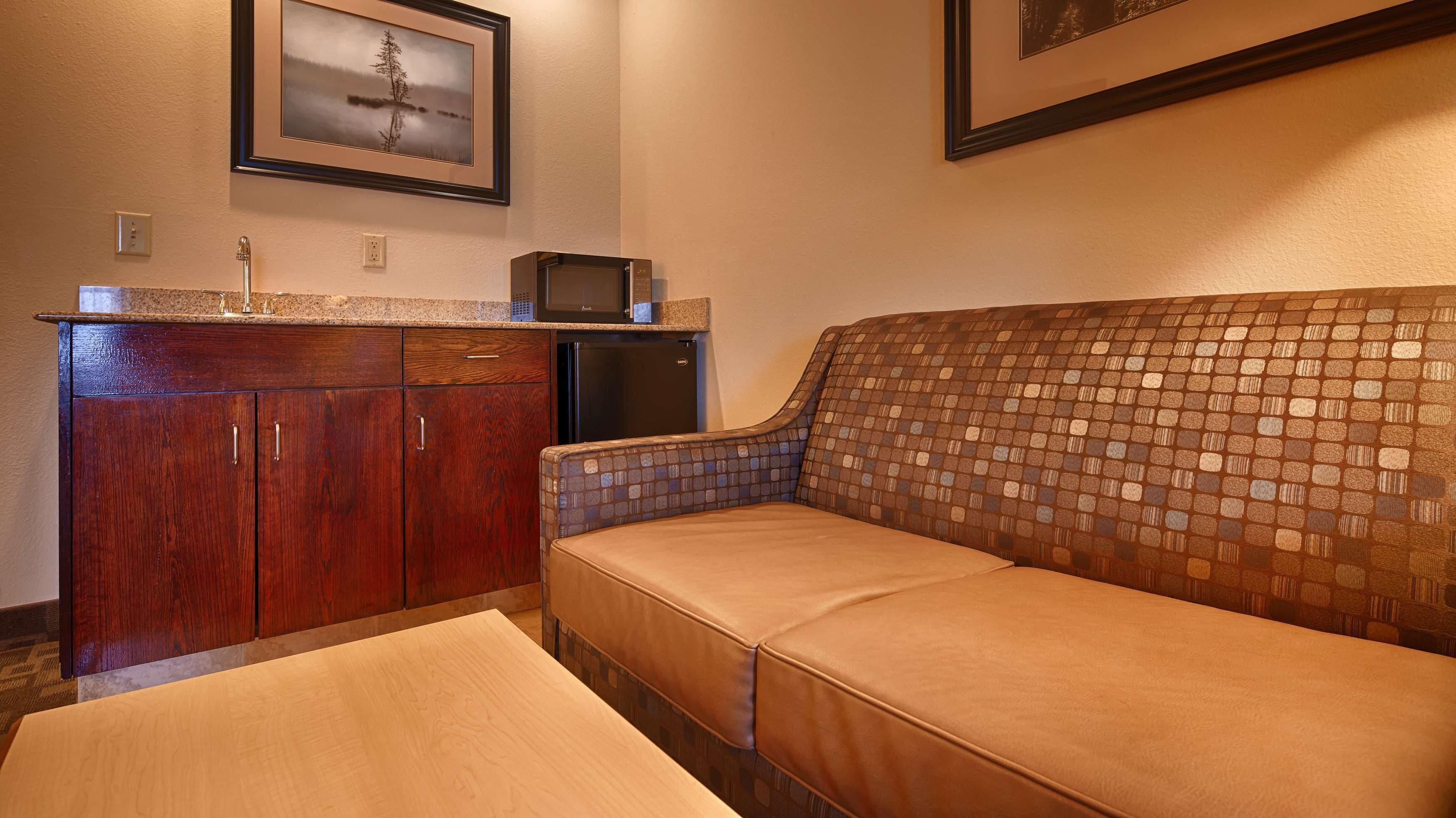 A compact room with a wooden cabinet, a microwave, a small refrigerator, and a cushioned seating area with a mosaic-patterned backrest.