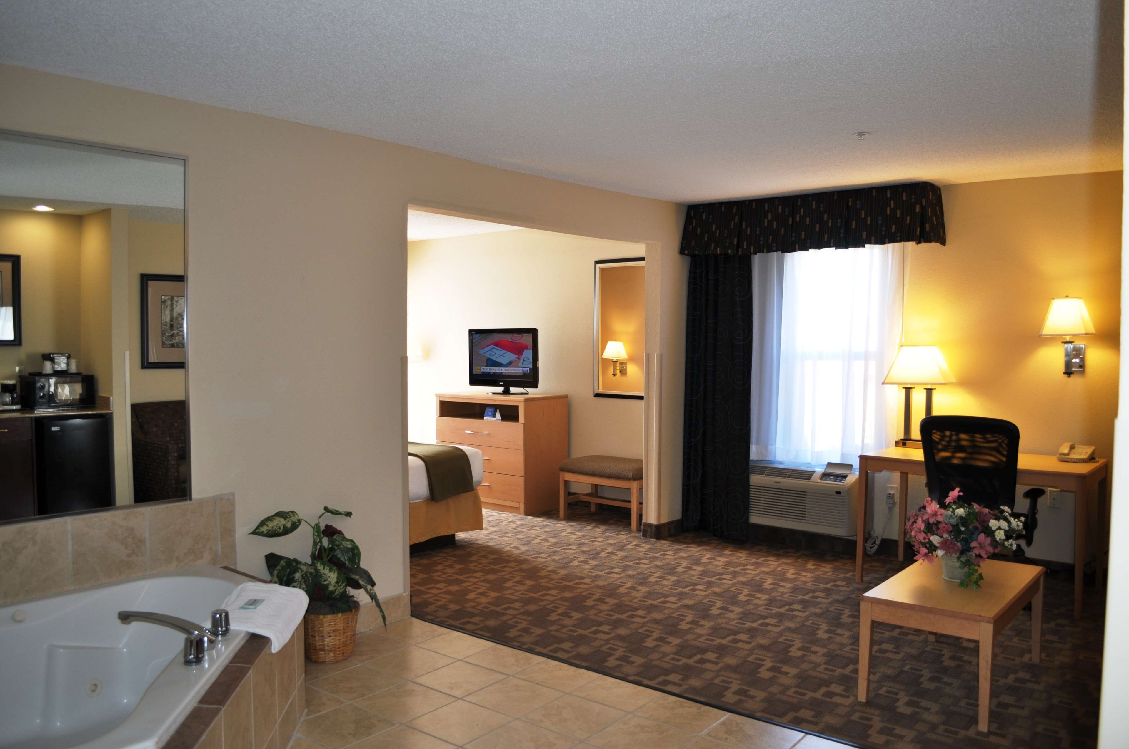 Habitación de hotel con baño, escritorio, silla, televisión y una pequeña mesa con un florero.