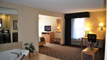 Habitación de hotel con baño, escritorio, silla, televisión y una pequeña mesa con un florero.