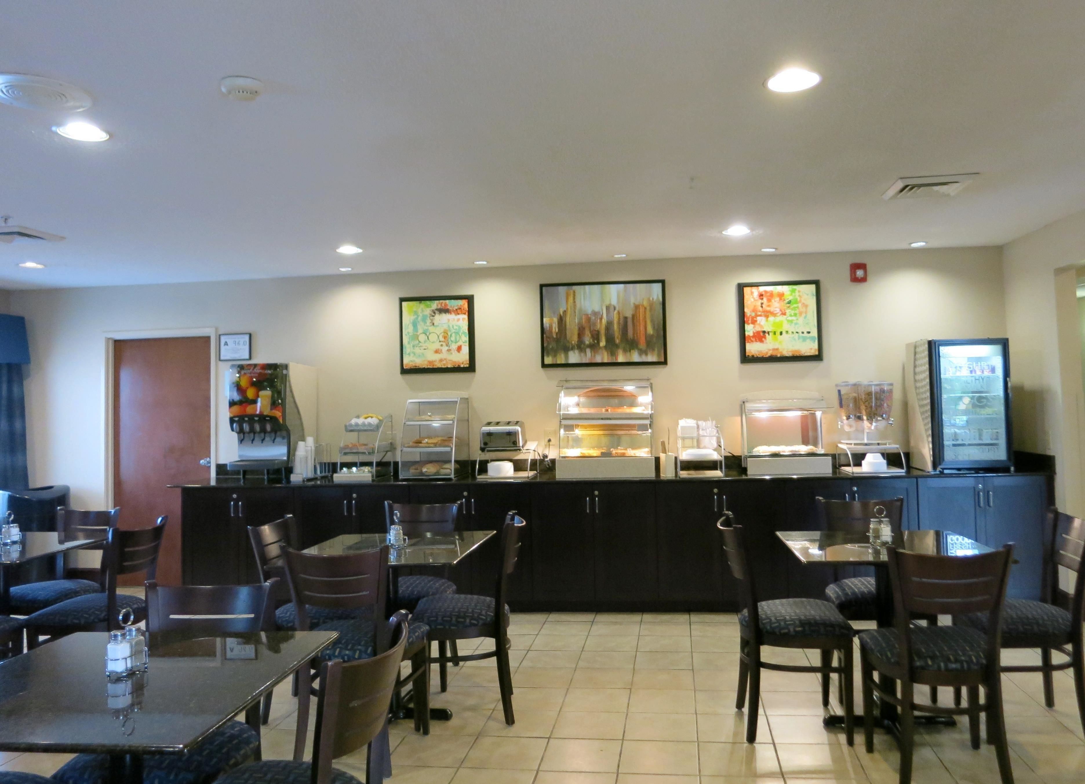 A hotel dining area with a buffet counter, chairs, tables, and artwork on the walls.