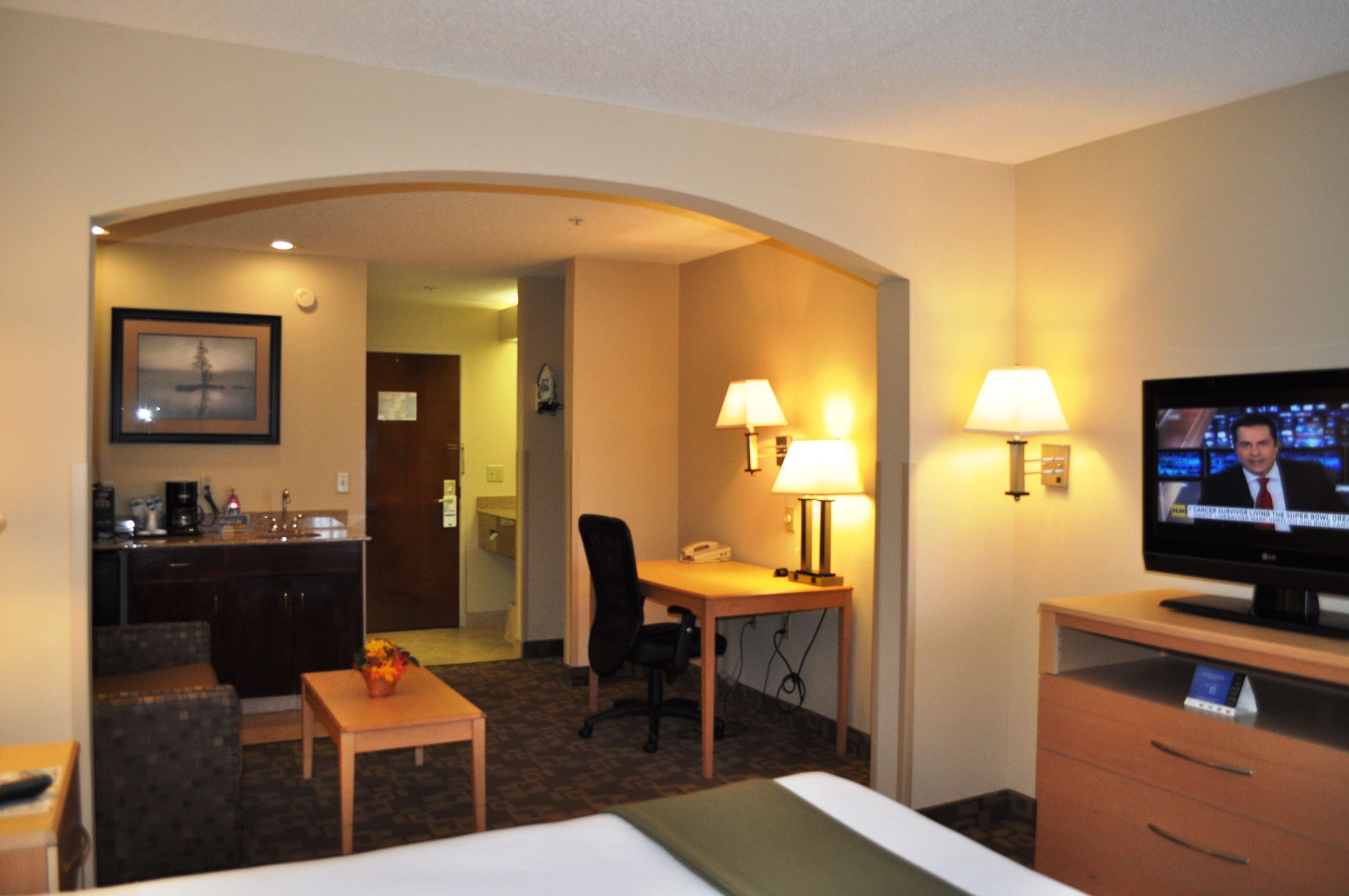 A hotel room with a bed, desk, chair, TV, and kitchenette.