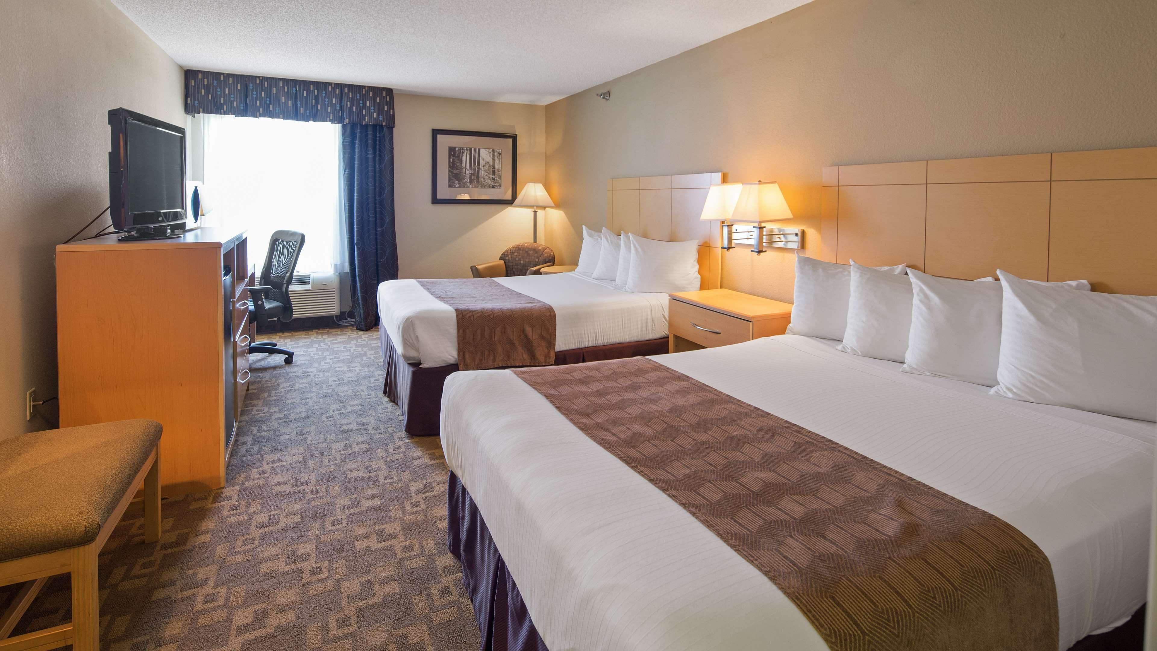 A hotel room with two beds, a desk, a chair, a television, and a picture on the wall.
