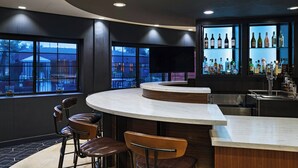 Zona de bar moderna con una barra curva, taburetes, una gran pantalla de televisión y una vitrina de vinos.