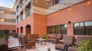 Un espacio al aire libre con varios sofás y mesas, luces colgantes y un edificio con balcones.