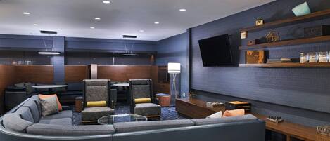 A modern living room with a sectional sofa, armchairs, a coffee table, and a flat-screen TV mounted on the wall.