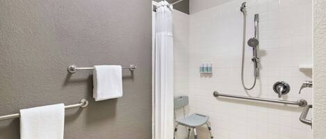 A shower area with a grab bar, a small step stool, and a showerhead.