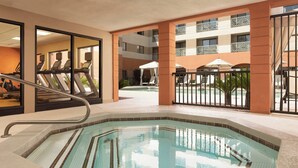 Zona de piscina de hotel con jacuzzi, equipo de ejercicios y sillones de descanso.