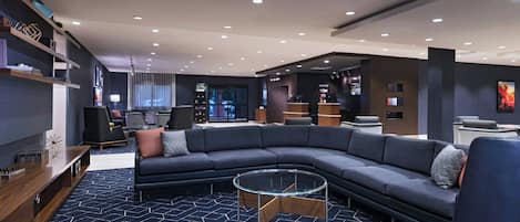 A modern living room with a sectional sofa, a glass coffee table, and a patterned carpet.