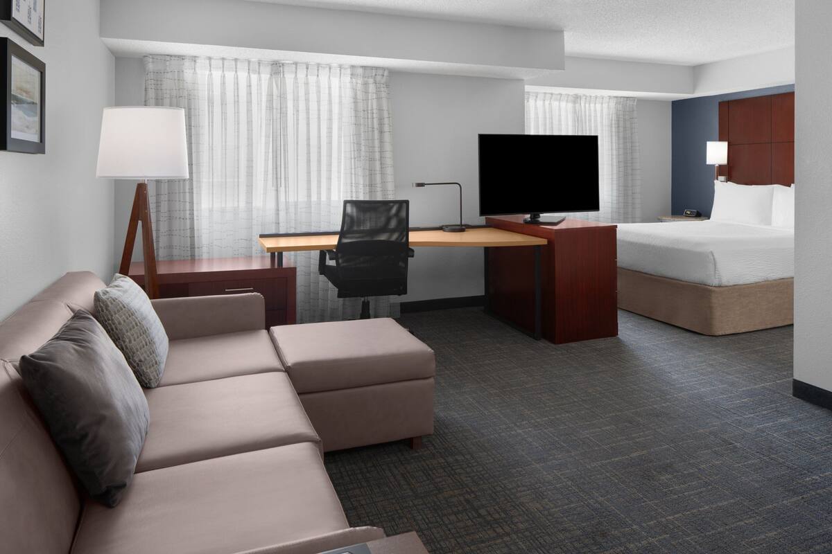 Een hotelkamer met een bed, een bureau met een televisie, een bank en een lamp.